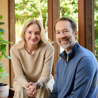 Wellmind's founders, Laura Beann (LCSW, and CEO & Clinical Director) and Earik Beann (CTO) sit beside one another smiling gently, surrounded by greenery.