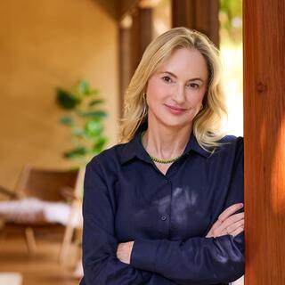 Laura Beann, LCSW, and Founder, CEO & Clinical Director of Wellmind smiles warmly, wearing a navy blue blouse against a warm, light-filled interior space.