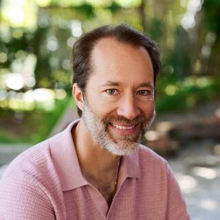 Earik Beann, Wellmind Founder and CTO smiles wearing a pink polo shirt against a lush green background.