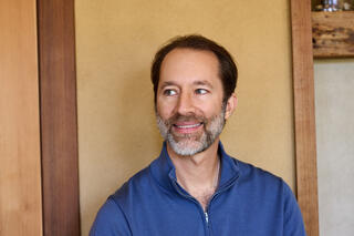 Earik Beann, Founder and CTO smiles against a rustic background, wearing a blue sweater.