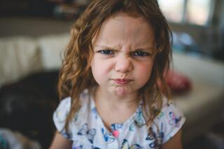 A young girl with curly hair furrows her brow and pouts, conveying a strong expression of frustration or discontent.