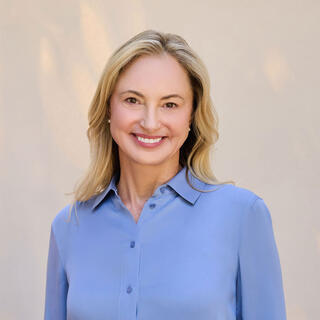 Laura Beann, LCSW, and Founder, CEO & Clinical Director of Wellmind smiles warmly, wearing a light blue blouse against a soft, neutral background. Her hair cascades in gentle waves.